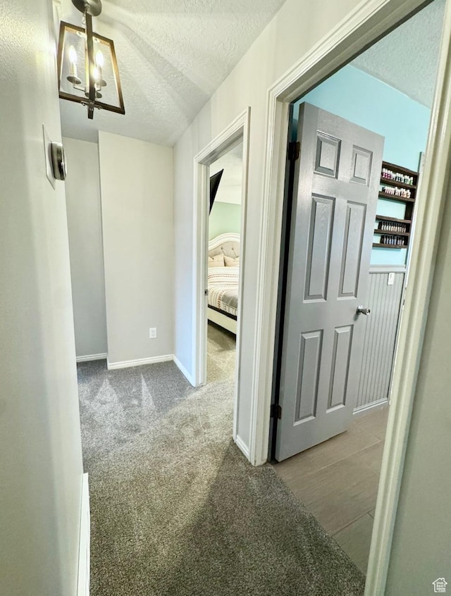 hall with carpet floors, a textured ceiling, baseboards, and an inviting chandelier