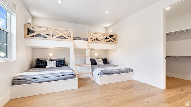 bedroom featuring a walk in closet, a closet, wood finished floors, and recessed lighting
