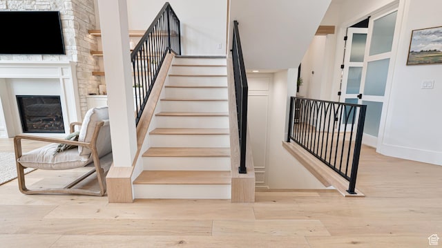 stairway with a glass covered fireplace, wood finished floors, and baseboards