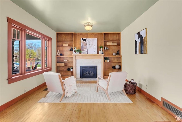 living area with wood-type flooring, a tiled fireplace, visible vents, and baseboards