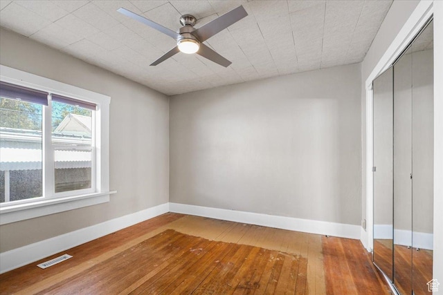 unfurnished bedroom with visible vents, a ceiling fan, a closet, baseboards, and hardwood / wood-style flooring