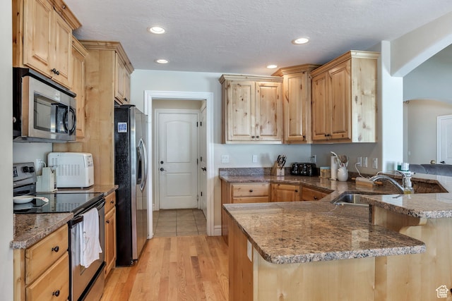 kitchen with stainless steel appliances, a peninsula, a sink, arched walkways, and light brown cabinets