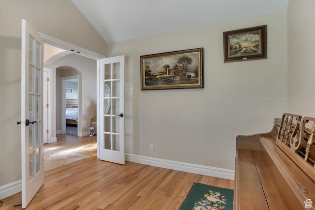 hallway featuring french doors, vaulted ceiling, arched walkways, and light wood-style floors