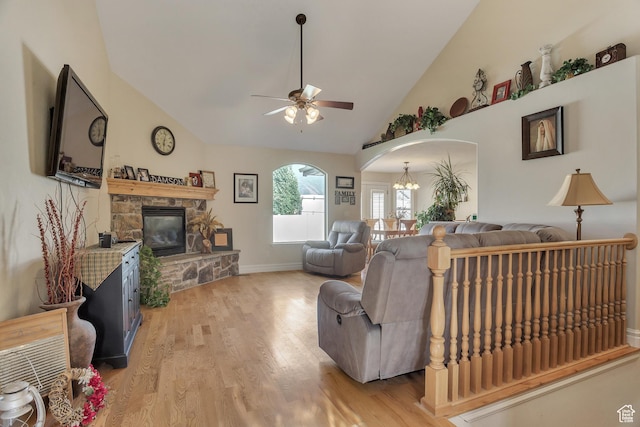 living area with arched walkways, a fireplace, light wood-style flooring, high vaulted ceiling, and ceiling fan with notable chandelier