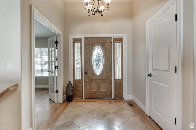 foyer entrance featuring visible vents, light wood finished floors, baseboards, and an inviting chandelier