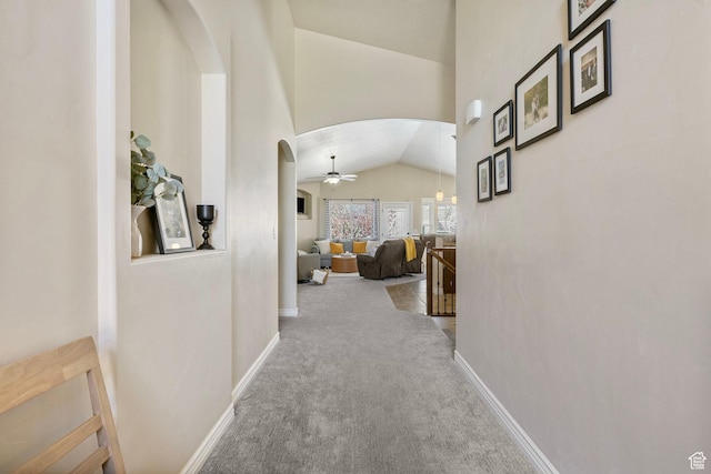 hallway featuring vaulted ceiling, baseboards, arched walkways, and carpet floors