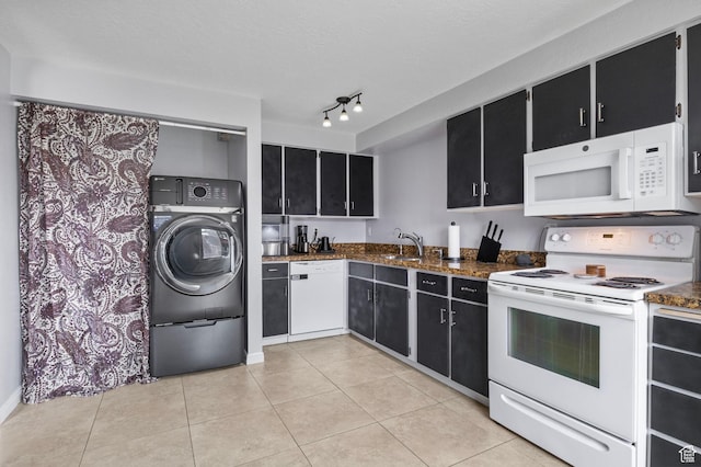 kitchen featuring dark stone counters, white appliances, light tile patterned floors, dark cabinetry, and washer / clothes dryer