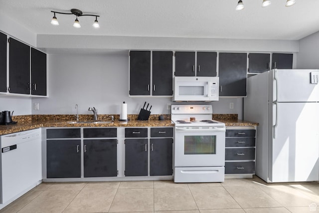 kitchen featuring dark cabinets, light tile patterned floors, a sink, and white appliances