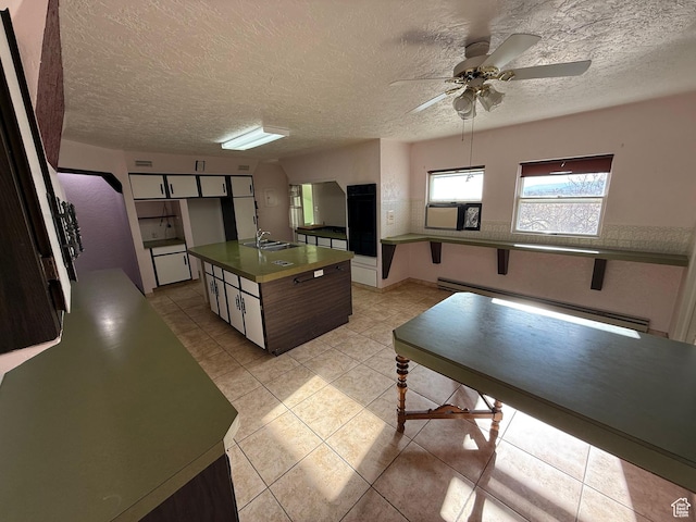kitchen with a ceiling fan, dark countertops, a sink, a baseboard heating unit, and light tile patterned floors