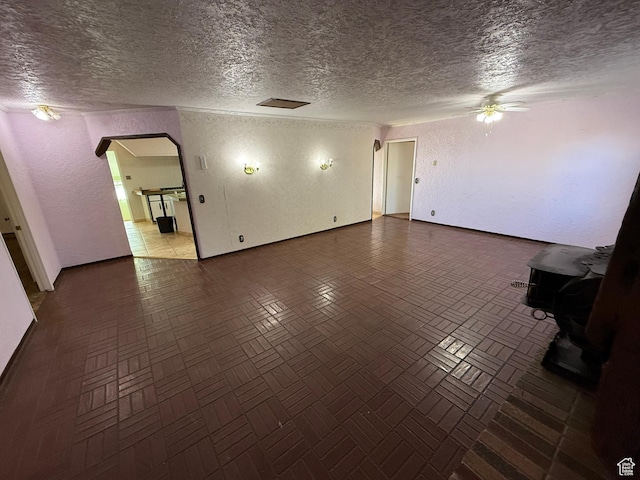 unfurnished living room featuring a textured wall, arched walkways, a ceiling fan, and a textured ceiling
