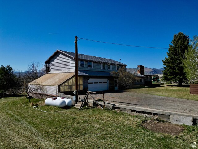 back of property featuring a yard, dirt driveway, and a garage