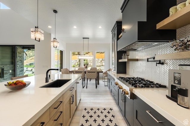 kitchen featuring open shelves, a sink, custom exhaust hood, light countertops, and tasteful backsplash