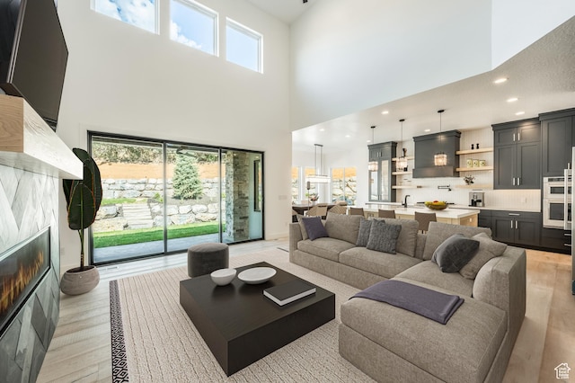 living area featuring a towering ceiling, light wood finished floors, a fireplace, and recessed lighting