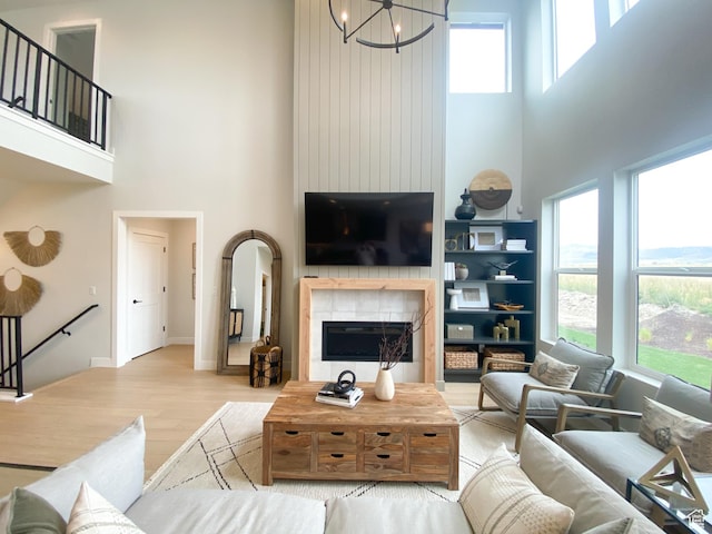 living area with wood finished floors, a large fireplace, a towering ceiling, baseboards, and a notable chandelier