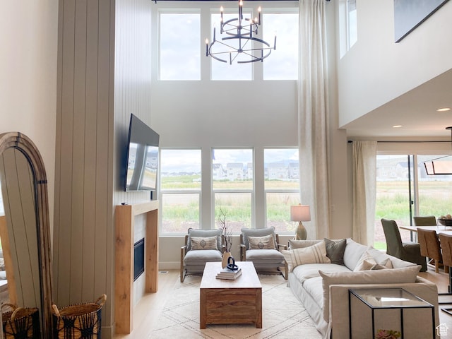 living area with a glass covered fireplace, light wood finished floors, a towering ceiling, and a notable chandelier
