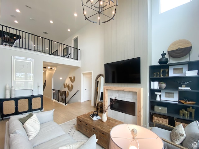 living area featuring a tiled fireplace, wood finished floors, a high ceiling, and recessed lighting