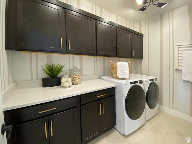 clothes washing area with a decorative wall, separate washer and dryer, light tile patterned flooring, cabinet space, and baseboards
