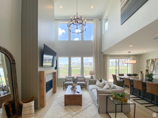 living room featuring a towering ceiling, a glass covered fireplace, recessed lighting, and a notable chandelier