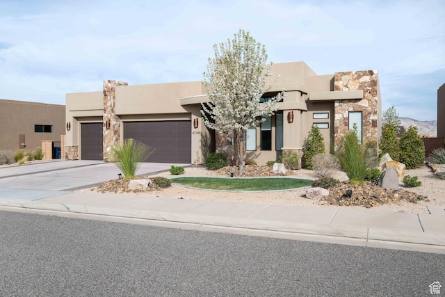 pueblo-style home with a garage, stone siding, concrete driveway, and stucco siding