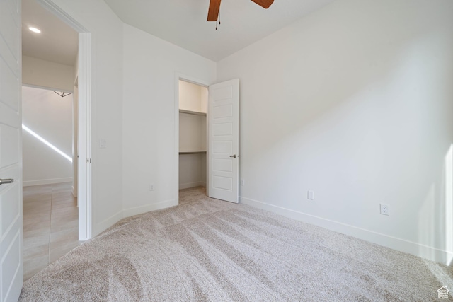 unfurnished bedroom featuring carpet floors, a spacious closet, baseboards, and ceiling fan