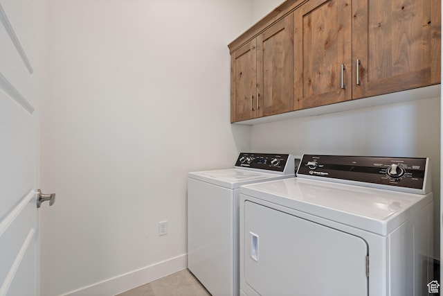 clothes washing area with washing machine and dryer, baseboards, and cabinet space