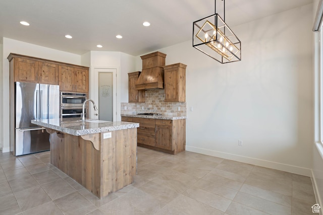 kitchen with light stone counters, a sink, decorative backsplash, premium range hood, and appliances with stainless steel finishes