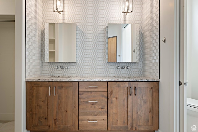 full bath featuring double vanity, toilet, a sink, baseboards, and tasteful backsplash