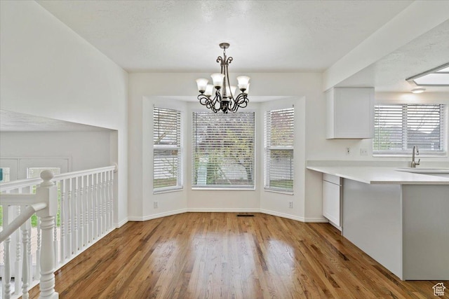 unfurnished dining area with a sink, visible vents, baseboards, a chandelier, and wood finished floors