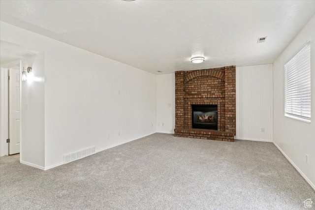 unfurnished living room featuring a brick fireplace, baseboards, carpet flooring, and visible vents