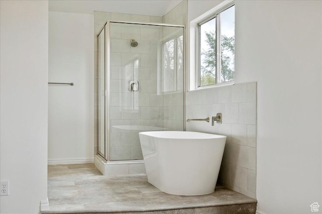 full bathroom with a shower stall, a freestanding bath, wood finished floors, and tile walls