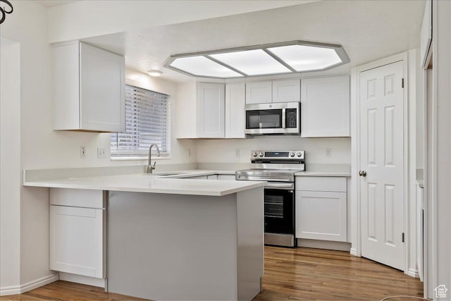kitchen featuring white cabinets, a peninsula, appliances with stainless steel finishes, and wood finished floors