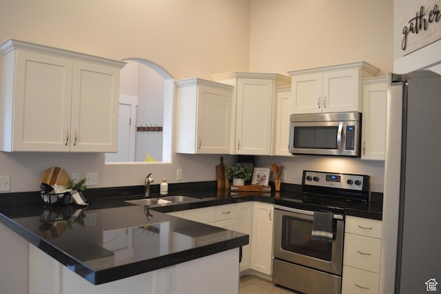 kitchen with a peninsula, white cabinetry, stainless steel appliances, and a sink