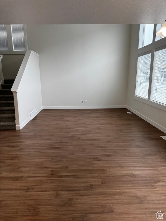 unfurnished living room featuring baseboards, dark wood-type flooring, and visible vents