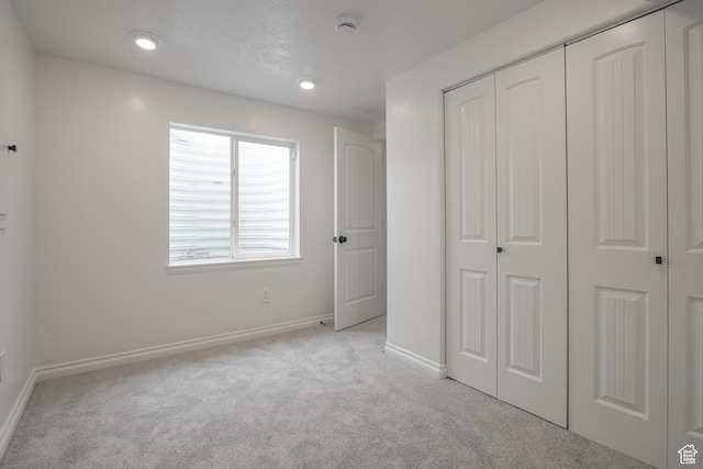 unfurnished bedroom with light carpet, a closet, and baseboards