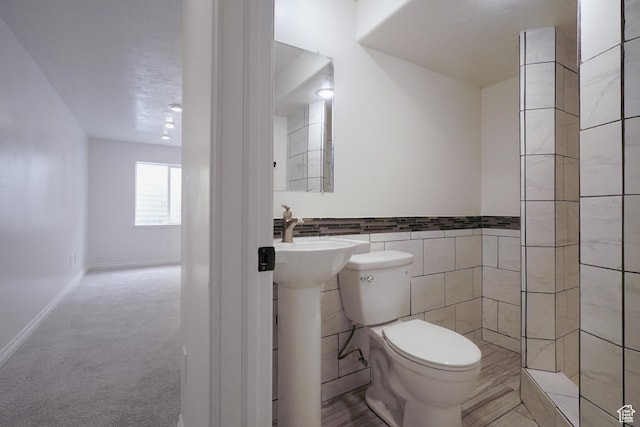 bathroom featuring toilet, a wainscoted wall, a sink, and tile walls