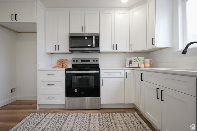 kitchen with light wood-type flooring, baseboards, white cabinetry, light countertops, and appliances with stainless steel finishes