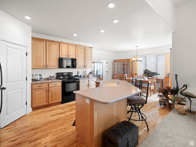 kitchen featuring black appliances, light wood-style flooring, a breakfast bar area, an inviting chandelier, and light countertops