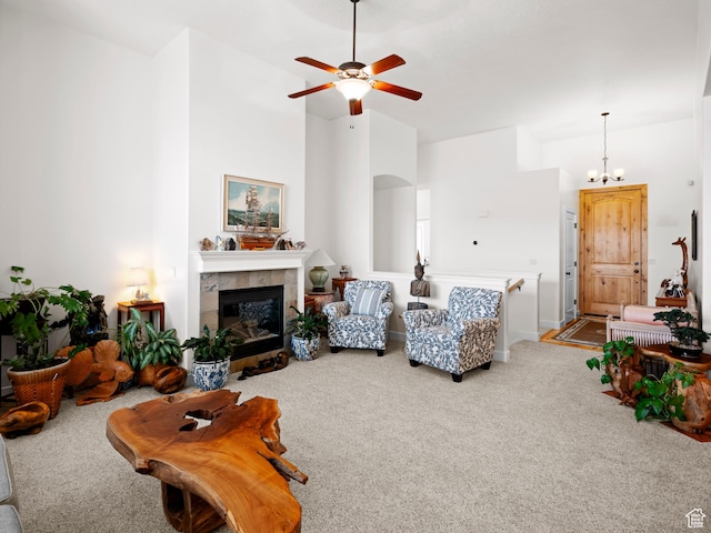 carpeted living area featuring ceiling fan with notable chandelier, a tiled fireplace, and high vaulted ceiling