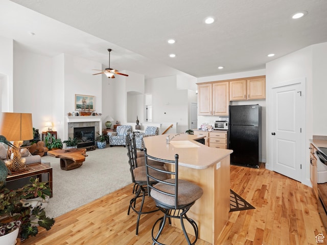 kitchen with light brown cabinets, black appliances, a sink, and light wood-type flooring