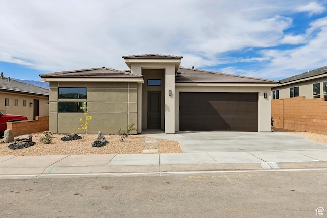 prairie-style house featuring a tile roof, concrete driveway, fence, an attached garage, and stucco siding