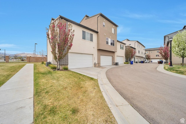 exterior space with a front lawn, an attached garage, fence, stucco siding, and a residential view