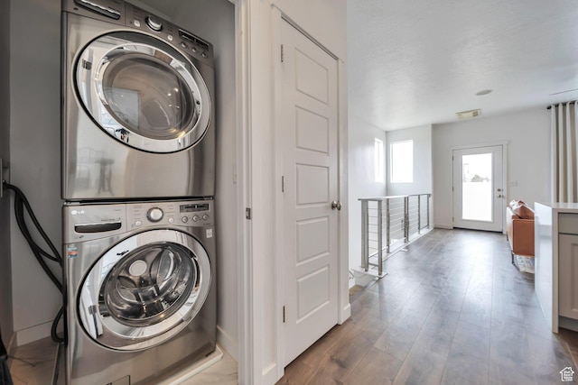laundry room with wood finished floors, laundry area, baseboards, stacked washer and clothes dryer, and visible vents