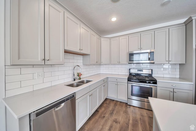 kitchen featuring dark wood finished floors, light countertops, a sink, gray cabinetry, and appliances with stainless steel finishes