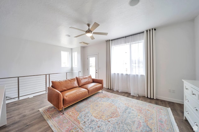 living area featuring a ceiling fan, a textured ceiling, visible vents, baseboards, and dark wood-style floors