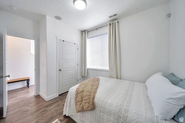 bedroom with dark wood-style floors, baseboards, a textured ceiling, and visible vents