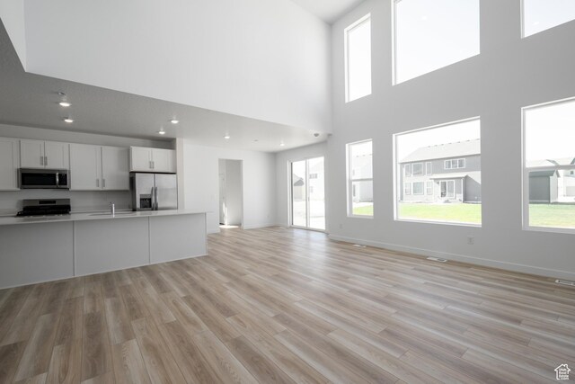 1784 E Bison Dr Unit B234, Eagle Mountain, UT 84005 - unfurnished living room featuring recessed lighting, a towering ceiling, a sink, light wood-style floors, and baseboards