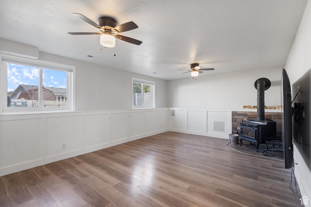 unfurnished living room with wood finished floors, a wood stove, ceiling fan, and visible vents