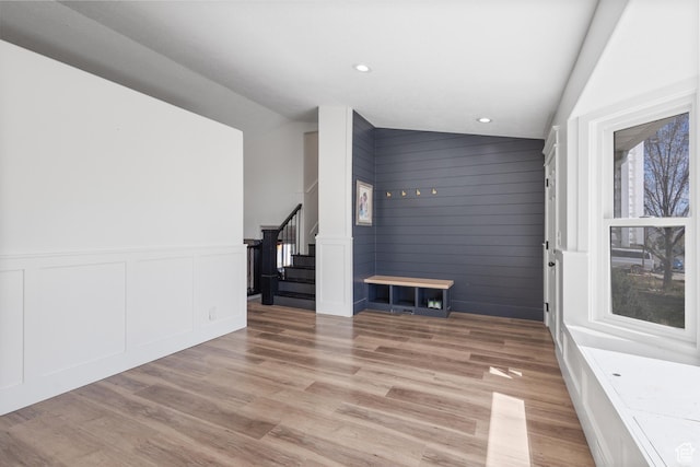 unfurnished living room featuring recessed lighting, vaulted ceiling, light wood-type flooring, a decorative wall, and stairs