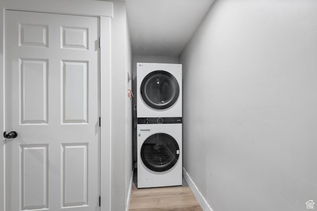 laundry room with stacked washer / drying machine, light wood finished floors, baseboards, and laundry area