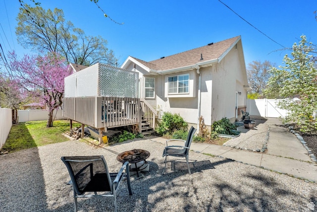 rear view of property featuring a gate, a fenced backyard, stucco siding, a wooden deck, and an outdoor fire pit